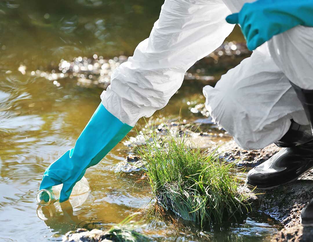 Mensch mit Labor Handschuhen nimmt eine Wasserprobe aus einem Fluss.