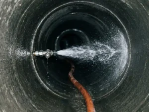 Hochdruckspülkopf im Einsatz in einem dunklen Betonkanal, orangefarbener Schlauch, Wasserstrahl glänzt an nassen Kanalwänden.