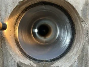 Innenansicht eines renovierten Abwasserrohrs mit glatter Auskleidung, sichtbarem Ablagerungsring am Eingang und warmem Inspektionslicht.