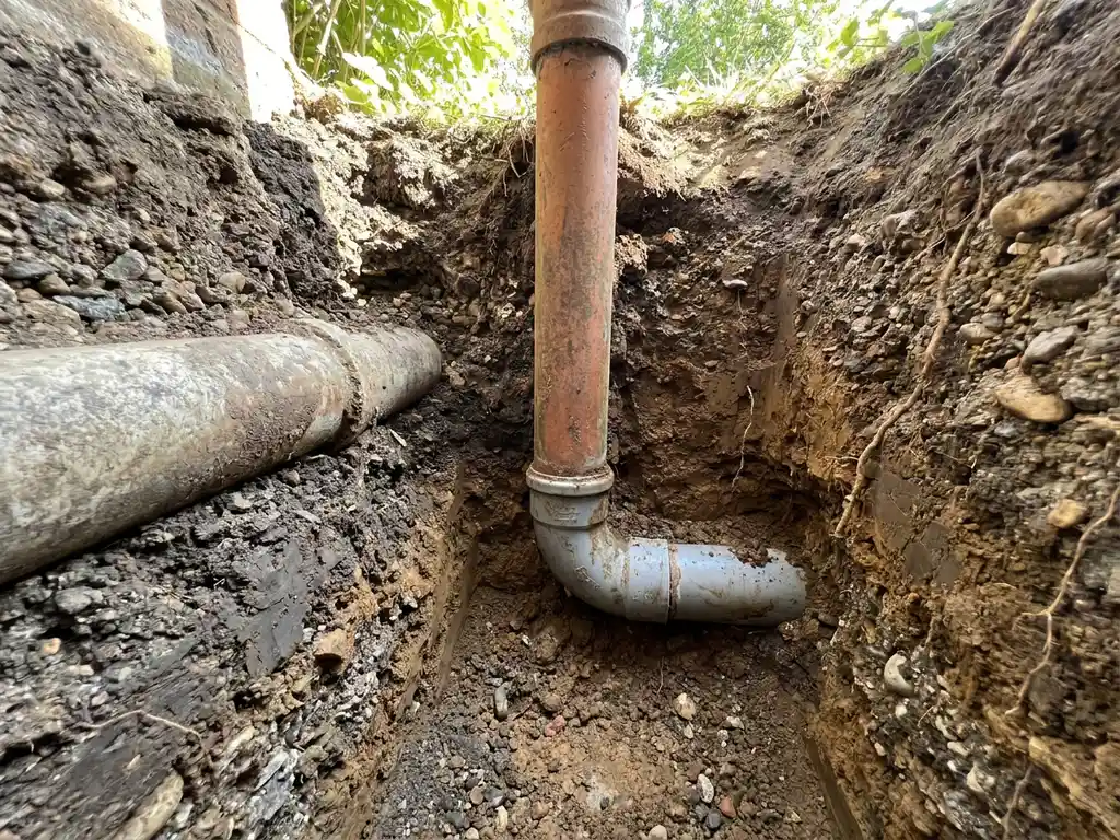 Querschnitt unterirdischer Drainagerohre aus PVC und Beton unter einem Hausgarten, eingebettet in Kies- und Lehmschichten.